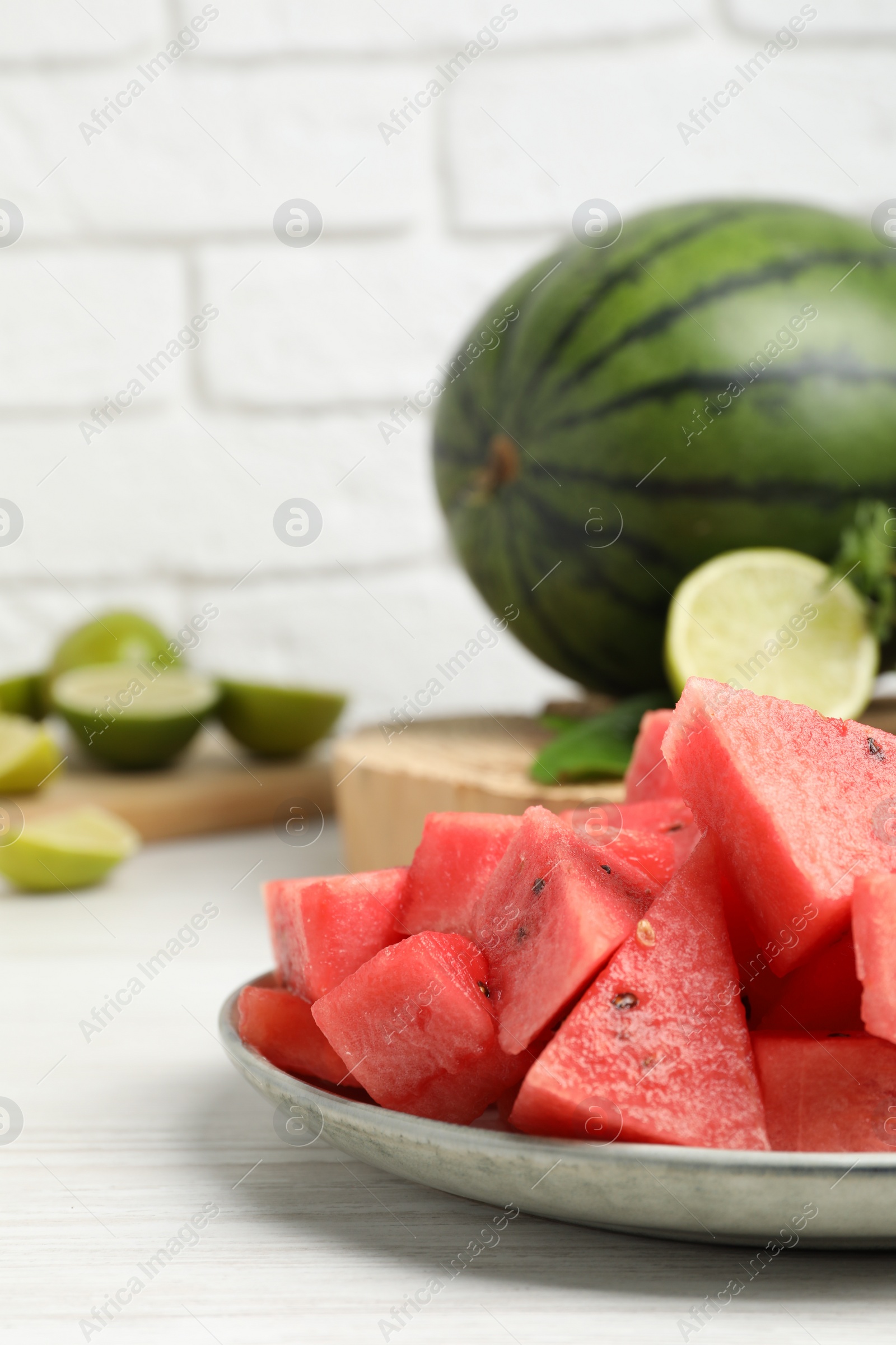 Photo of Slices of delicious watermelon and limes on white wooden table, space for text