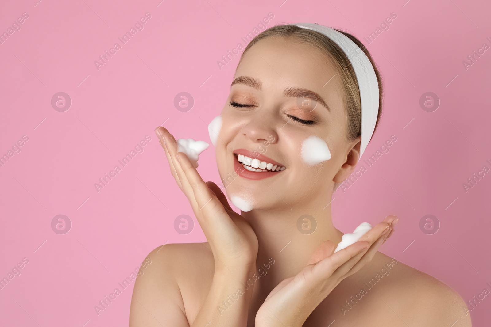 Photo of Young woman washing face with cleansing foam on pink background. Cosmetic product