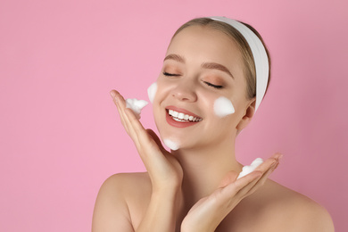 Young woman washing face with cleansing foam on pink background. Cosmetic product