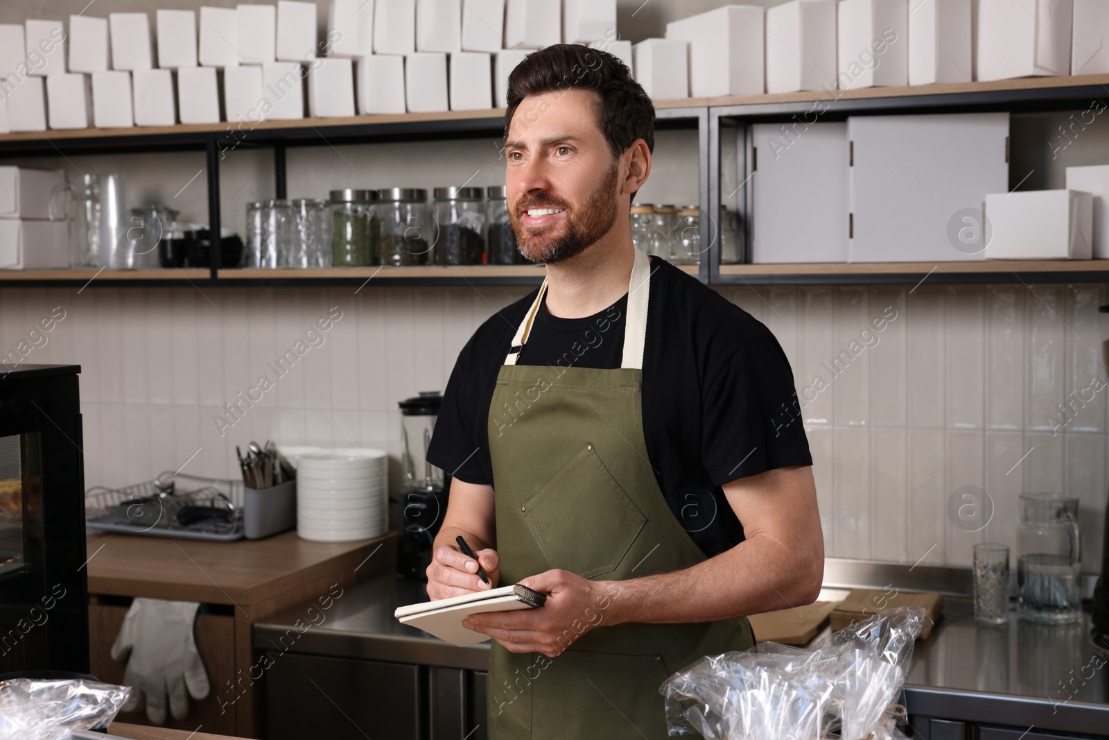 Photo of Happy seller with notebook and pen at cashier desk in bakery shop