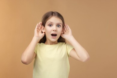 Little girl with hearing problem on pale brown background