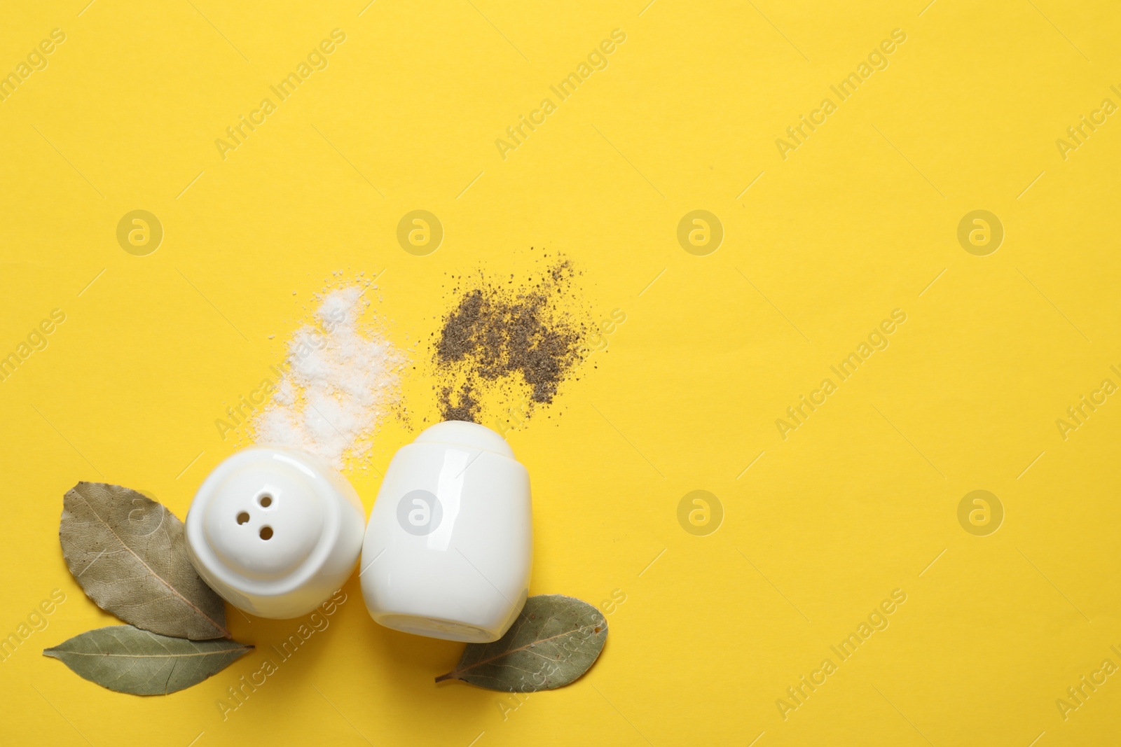 Photo of Salt and pepper shakers with bay leaves on yellow table, flat lay. Space for text