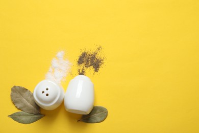 Photo of Salt and pepper shakers with bay leaves on yellow table, flat lay. Space for text