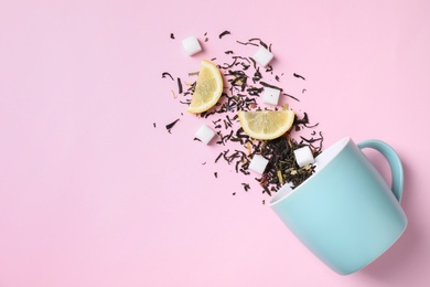Flat lay composition with overturned cup and dry tea leaves on pink background