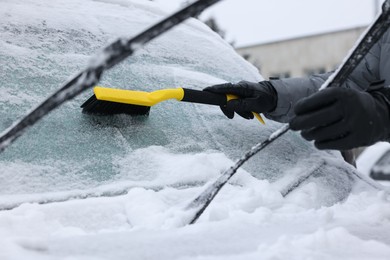 Photo of Man cleaning snow from car windshield outdoors, closeup