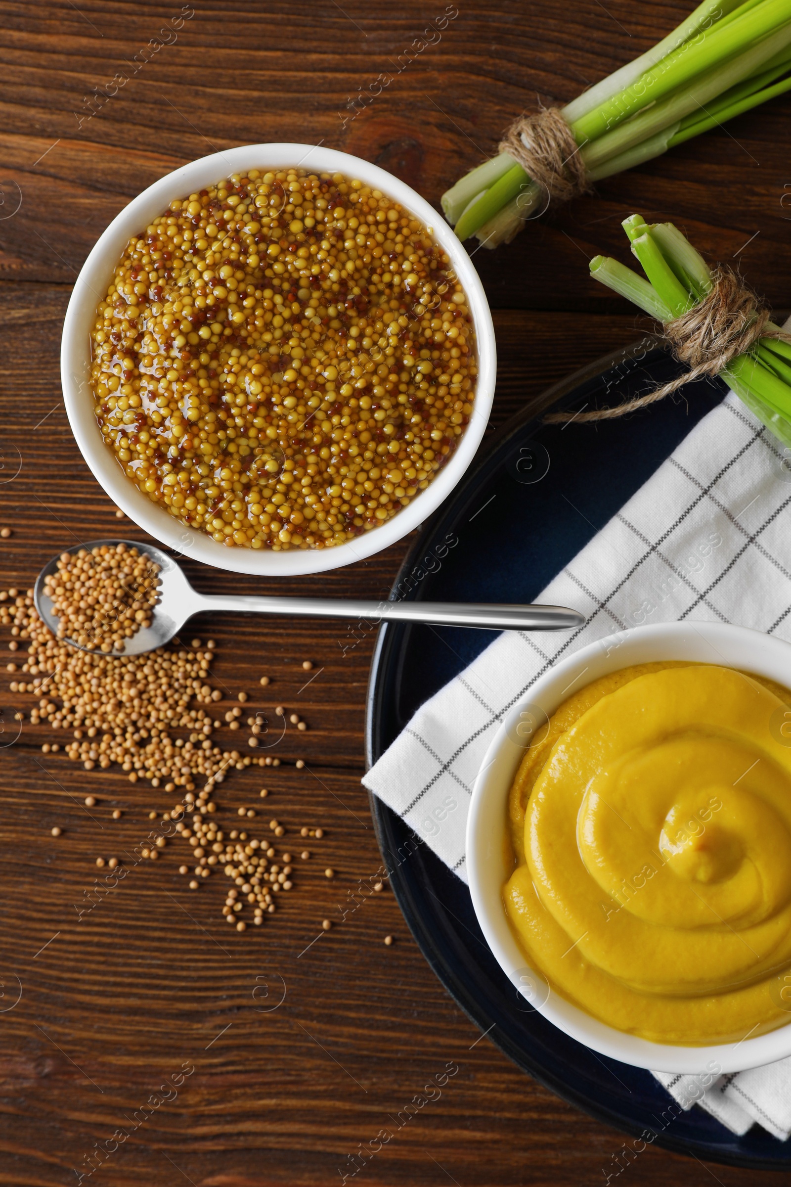 Photo of Delicious whole grain mustard, seeds and fresh green onion on wooden table, flat lay