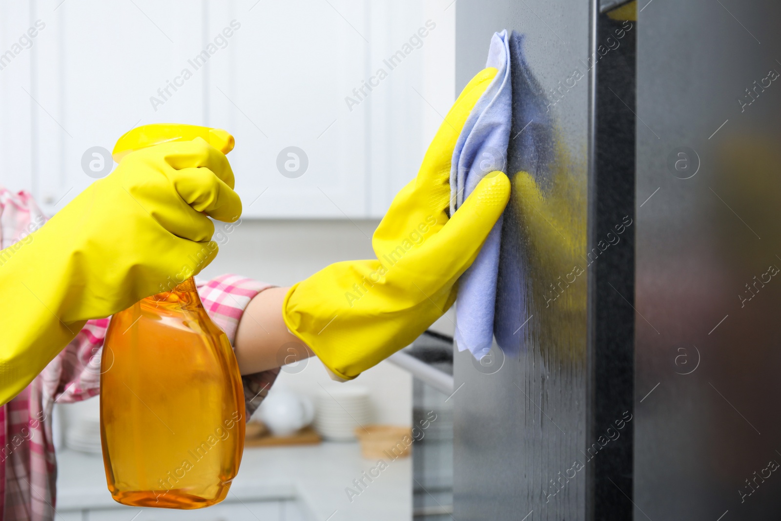 Photo of Woman cleaning fridge with rag and detergent indoors, closeup