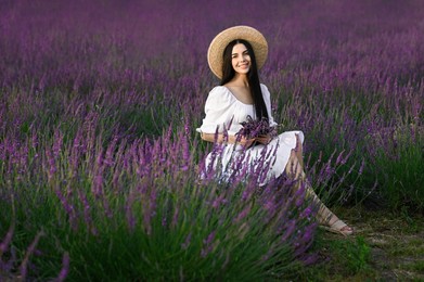 Photo of Beautiful young woman with bouquet sitting in lavender field