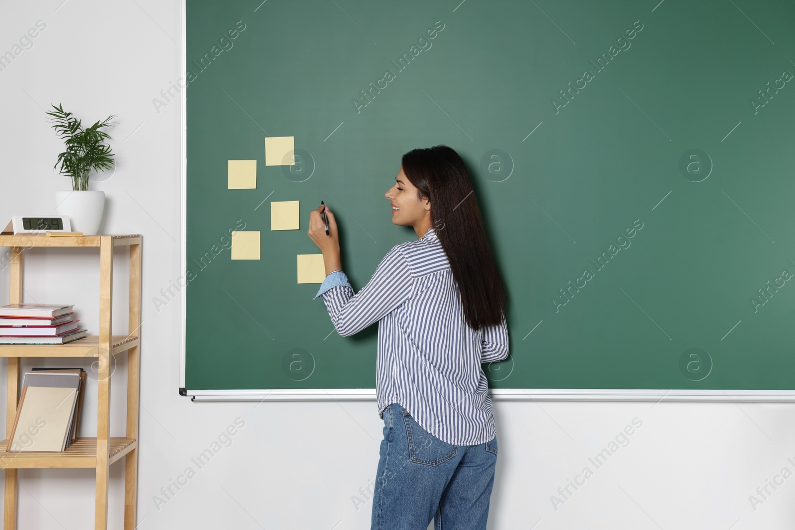 Photo of Happy young teacher giving lesson at blackboard in classroom. Space for text