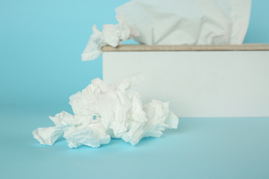 Photo of Used paper tissues and holder on light blue background, closeup