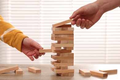 Photo of People playing Jenga tower at wooden table, closeup