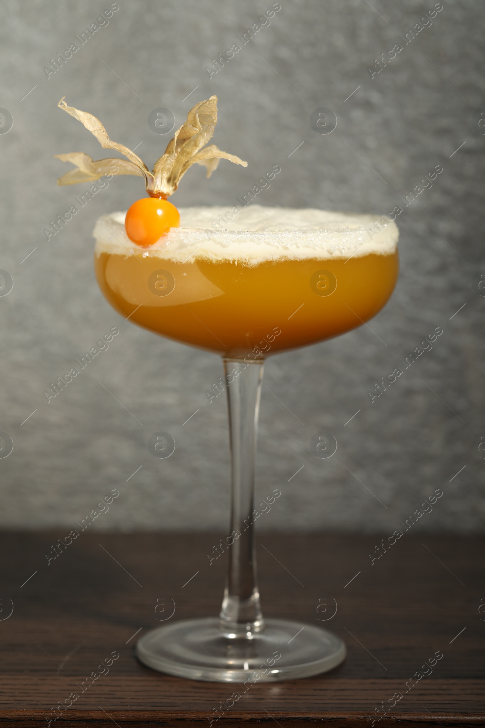 Photo of Refreshing cocktail decorated with physalis fruit on wooden table near grey wall