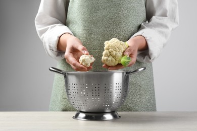 Photo of Woman separating fresh cauliflower cabbage above colander at wooden table, closeup