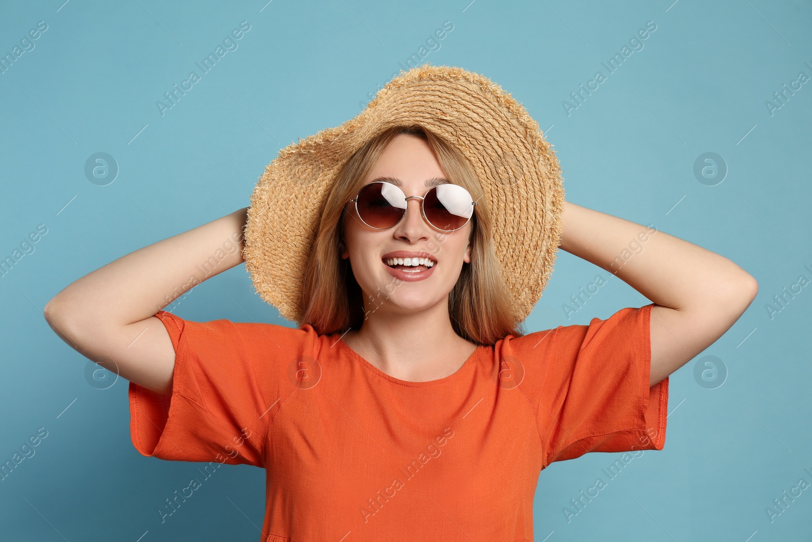 Photo of Beautiful young woman wearing straw hat and sunglasses on light blue background. Stylish headdress