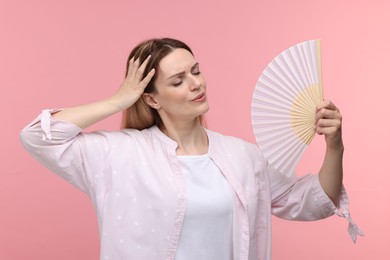 Photo of Beautiful woman waving hand fan to cool herself on pink background