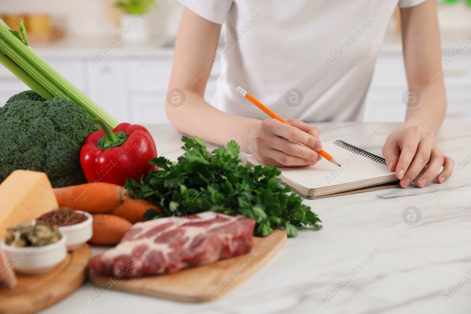 Photo of Woman with notebook and healthy food at white table, closeup. Keto diet