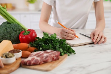 Woman with notebook and healthy food at white table, closeup. Keto diet