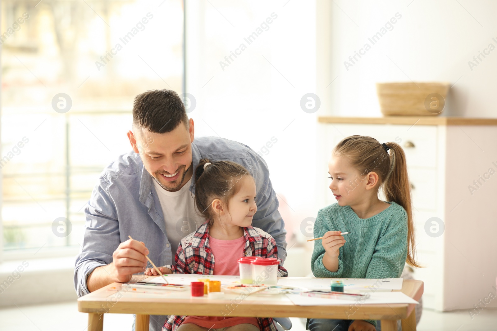 Photo of Father and daughters painting at table indoors. Playing with children