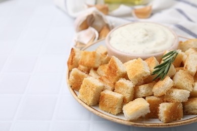 Photo of Delicious crispy croutons with rosemary and sauce on white tiled table, closeup
