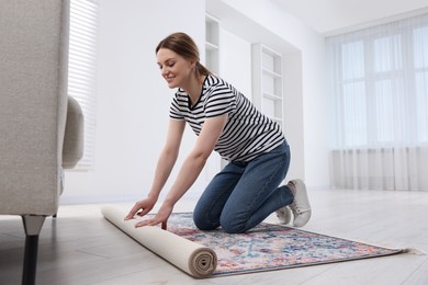 Photo of Smiling woman unrolling carpet with beautiful pattern on floor in room