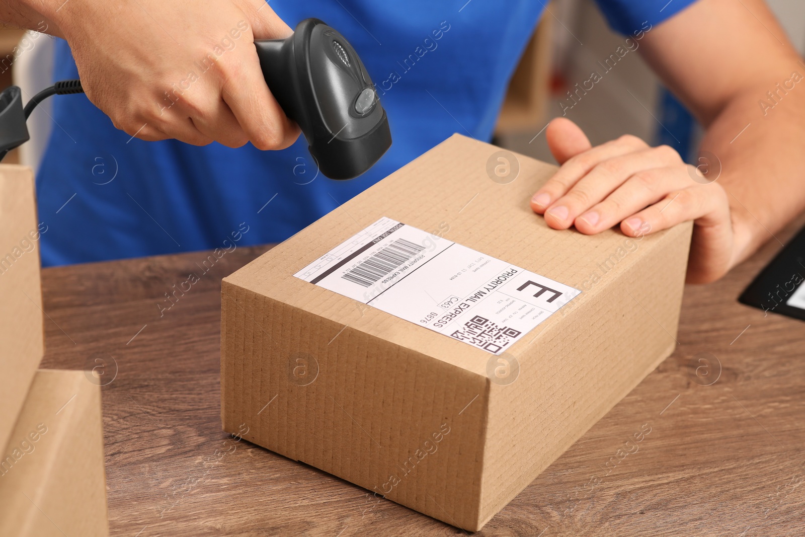 Photo of Post office worker with scanner reading parcel barcode at counter, closeup