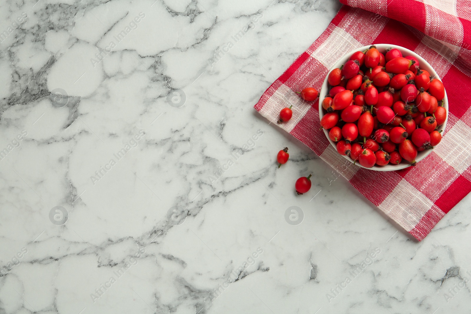 Photo of Ceramic bowl with rose hip berries, napkin and space for text on white marble table, flat lay. Cooking utensil