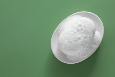 Dish with soap bar and fluffy foam on green background, top view. Space for text