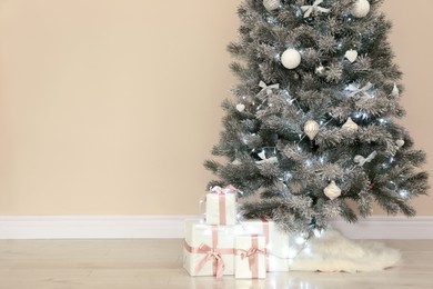Decorated Christmas tree with white faux fur skirt and gift boxes near beige wall. Space for text