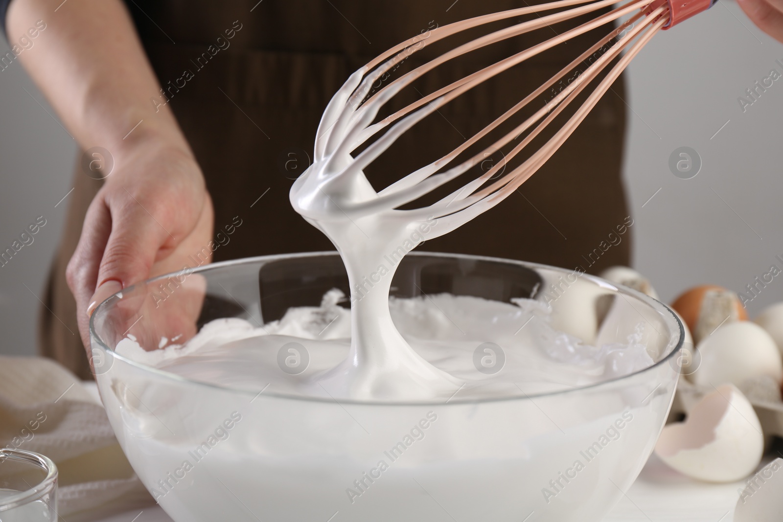 Photo of Woman making whipped cream with whisk at table, closeup