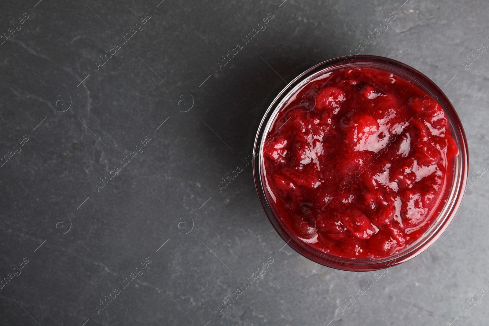 Photo of Bowl of cranberry sauce on grey background, top view. Space for text