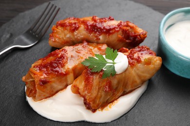 Photo of Delicious stuffed cabbage rolls served with sour cream on table, closeup
