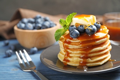 Delicious pancakes with fresh blueberries, butter and syrup on blue wooden table