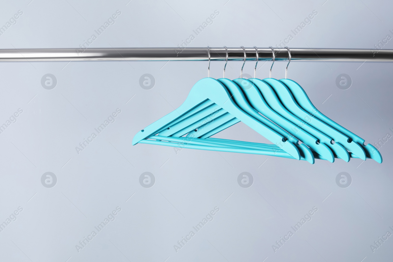 Photo of Clothes hangers on metal rail against color background