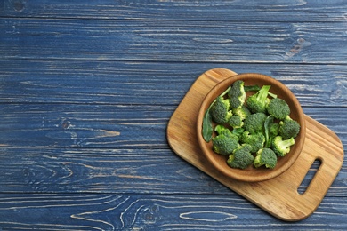 Photo of Bowl of fresh broccoli on blue wooden table, top view with space for text