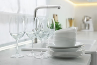 Photo of Different clean dishware and glasses on countertop near sink in kitchen