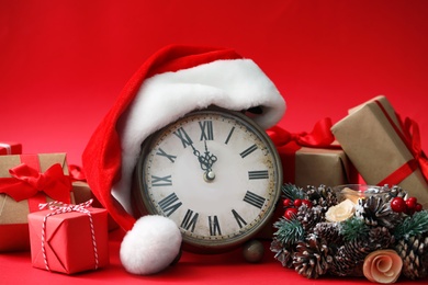 Photo of Alarm clock, gifts and festive decor on red background. New Year countdown