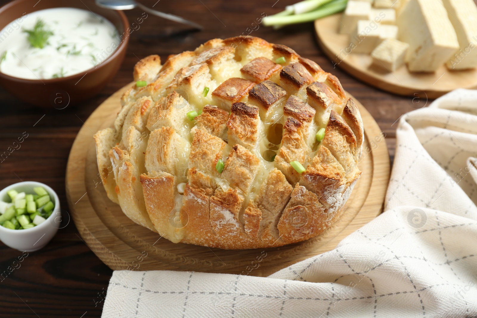 Photo of Freshly baked bread with tofu cheese, green onions and sauce on wooden table