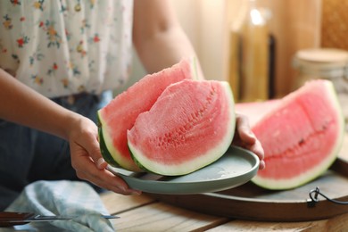 Photo of Woman holding plate with sliced fresh juicy watermelon over wooden table, closeup