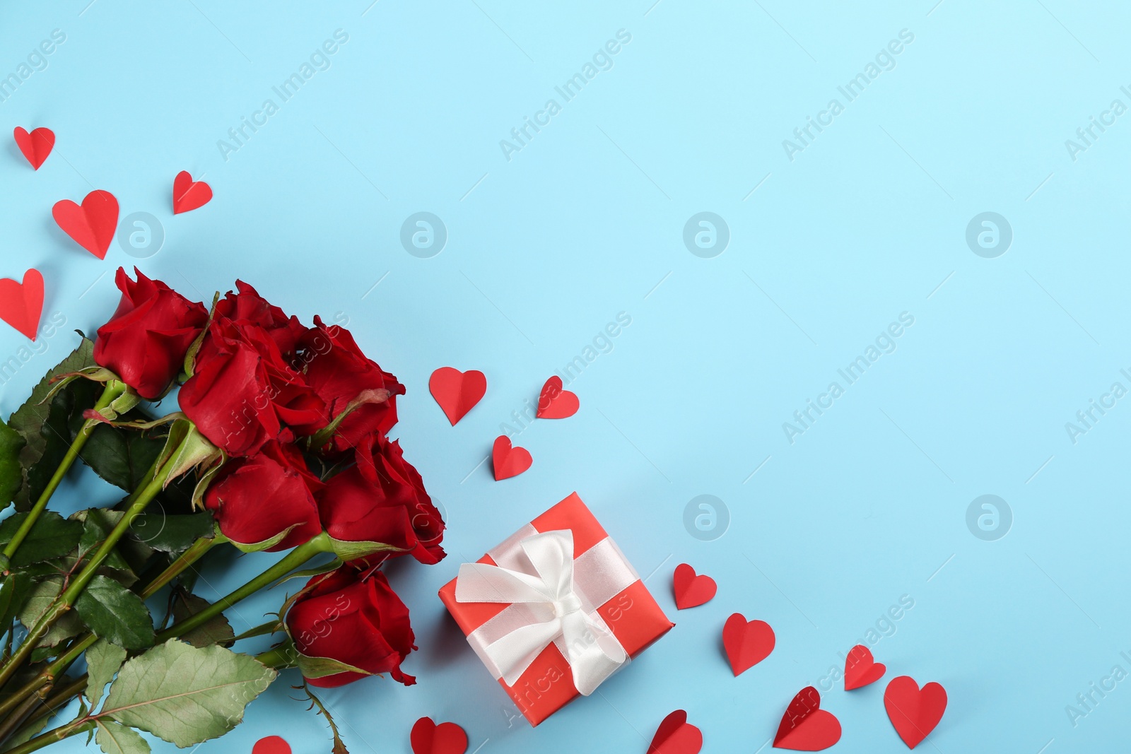 Photo of Beautiful red roses, gift box and paper hearts on light blue background, flat lay with space for text. Valentine's Day celebration