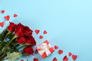 Photo of Beautiful red roses, gift box and paper hearts on light blue background, flat lay with space for text. Valentine's Day celebration