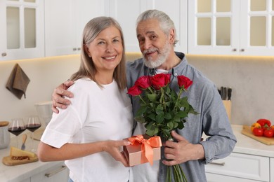 Photo of Happy affectionate senior couple with gift box and beautiful bouquet indoors