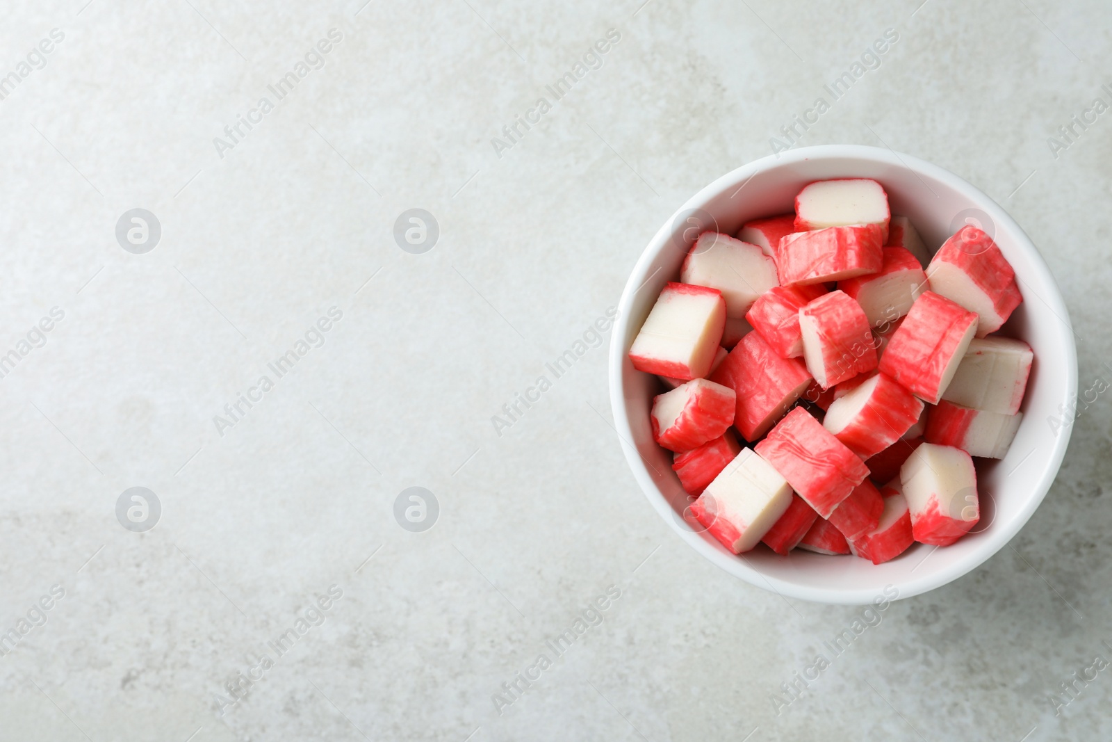 Photo of Cut crab sticks in bowl on light table, top view. Space for text