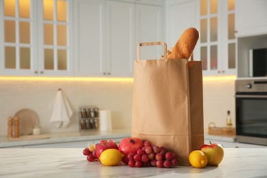 Paper shopping bag with baguette and fresh fruits on white marble table in kitchen. Space for text