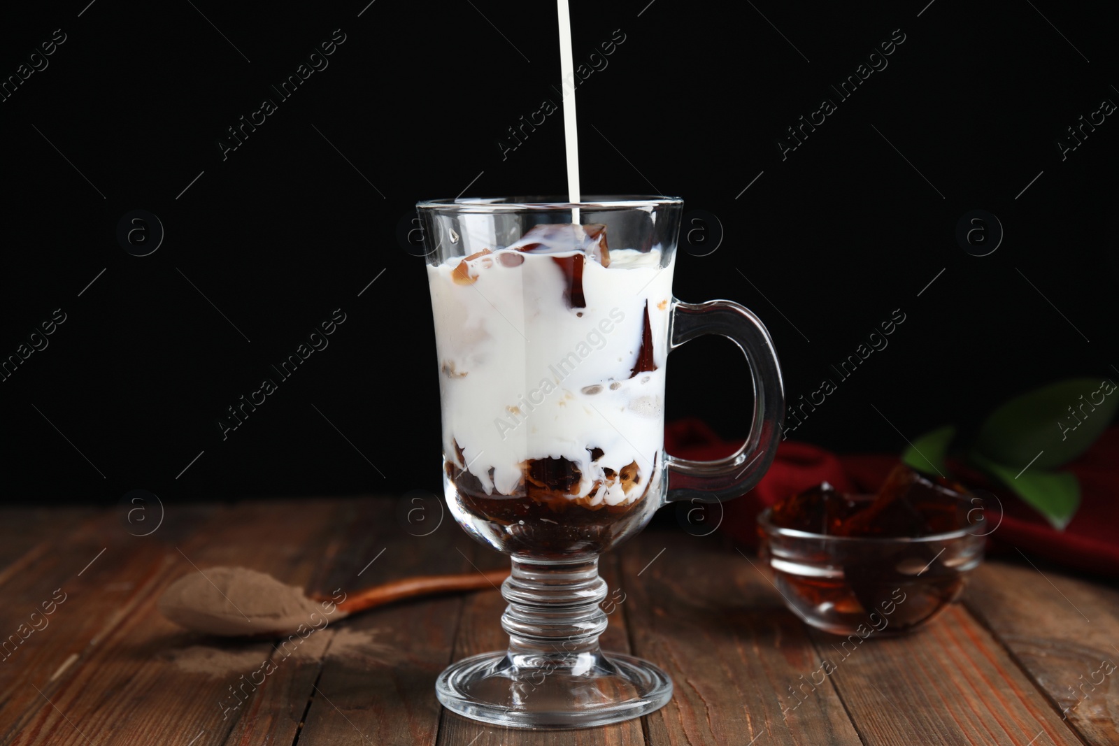 Photo of Pouring milk into glass cup with delicious grass jelly at wooden table