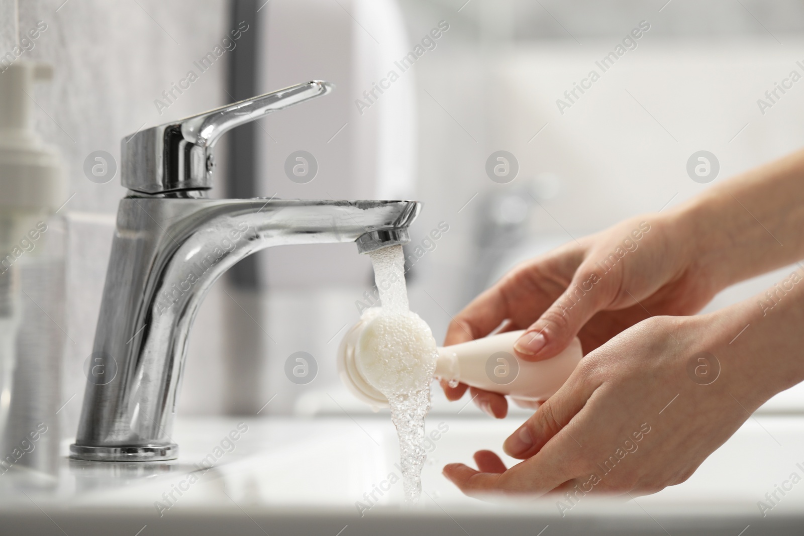 Photo of Young woman washing facial brush in bathroom, closeup