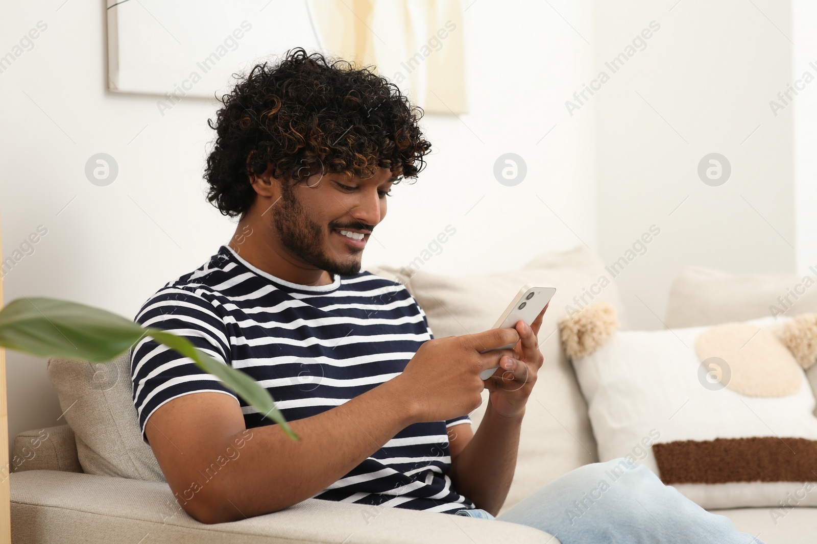 Photo of Handsome smiling man using smartphone in room, space for text