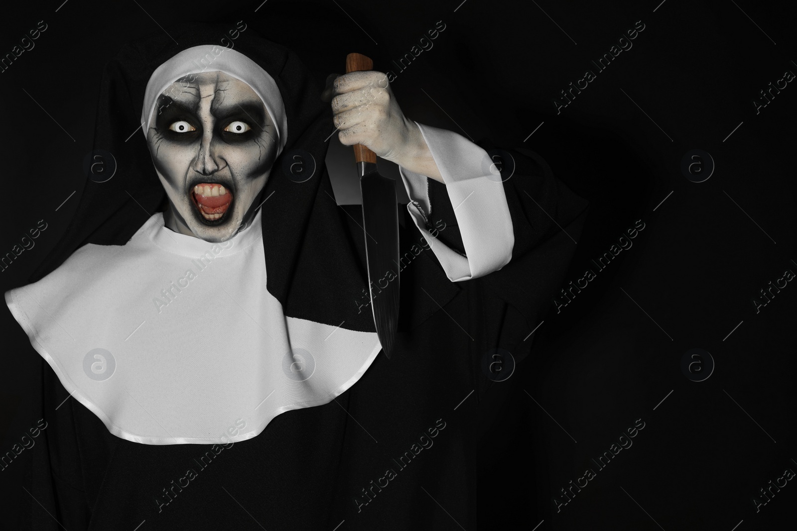 Photo of Scary devilish nun with knife on black background, space for text. Halloween party look