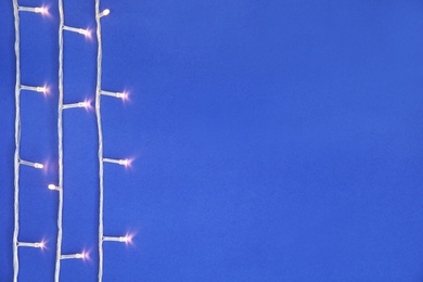 Photo of Glowing Christmas lights on color background, top view