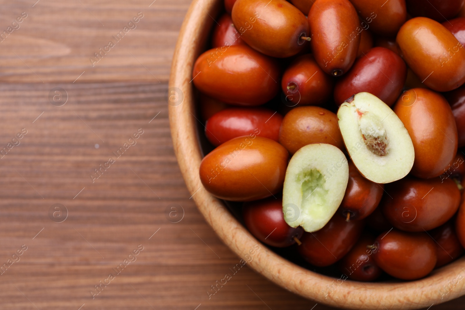 Photo of Fresh Ziziphus jujuba fruits in bowl on wooden table, top view. Space for text