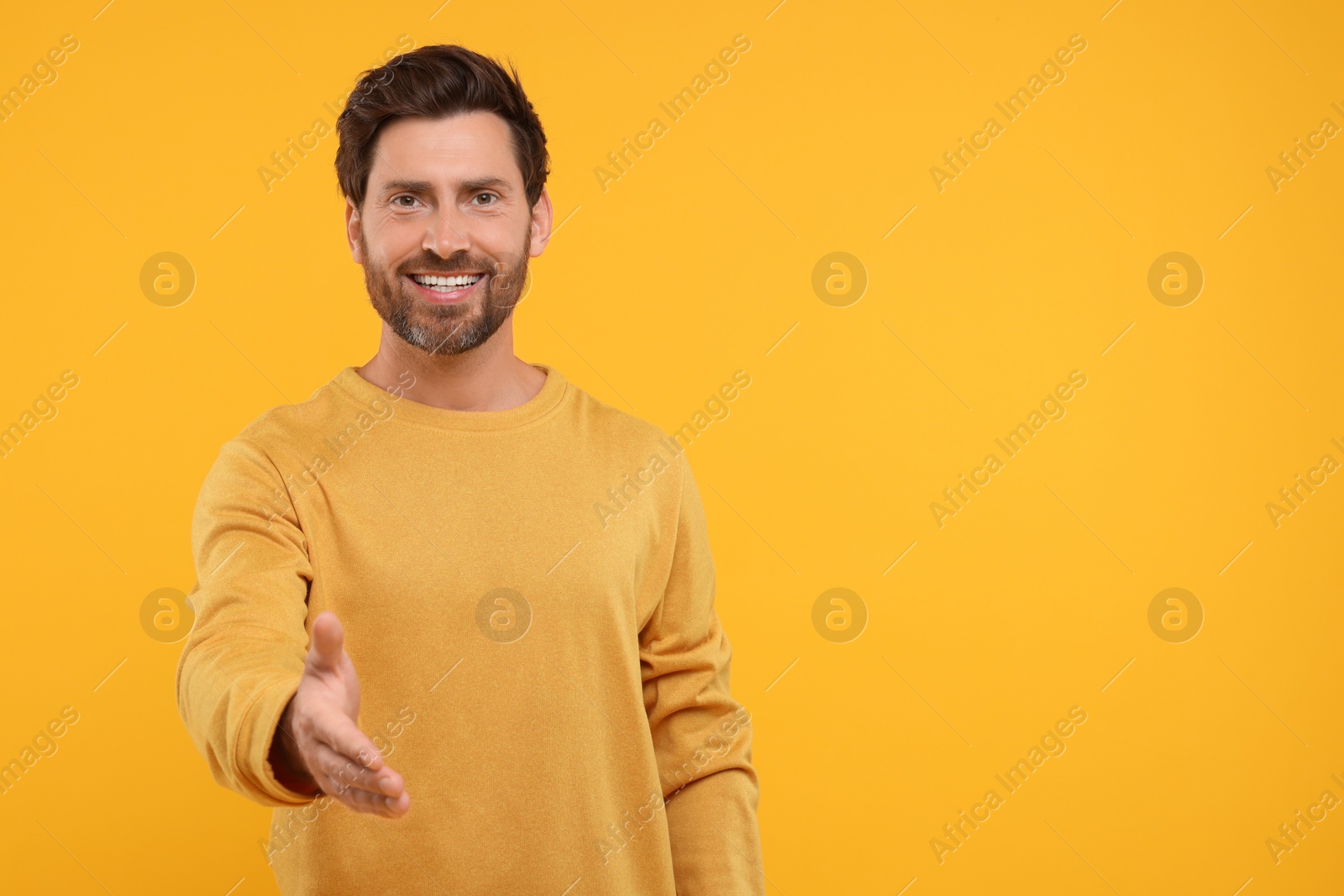 Photo of Happy man welcoming and offering handshake on orange background. Space for text